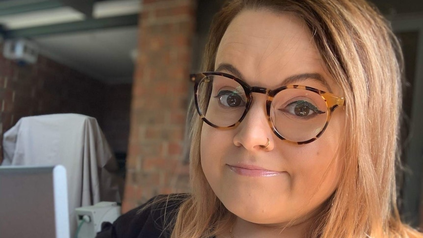 A woman in her 30s with glasses with brown hair looking at the camera with a bemused look