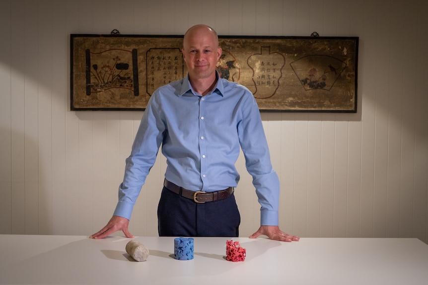 A man wearing a blue shirt stands behind table