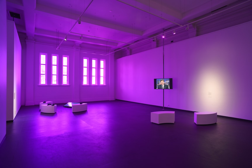 A large, mostly empty space in an art gallery, bathed in purple light.