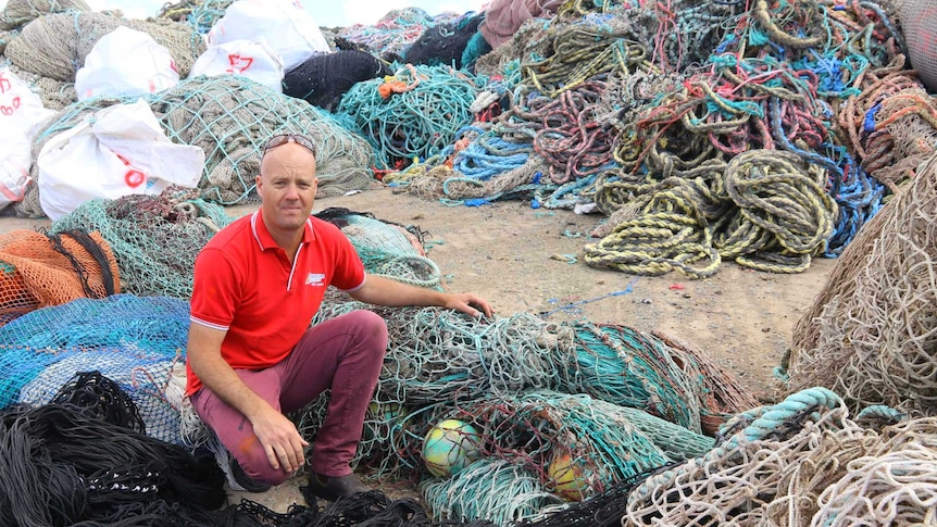 Man crouching in front of piles of fishing netting