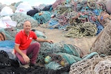 Man crouching in front of piles of fishing netting