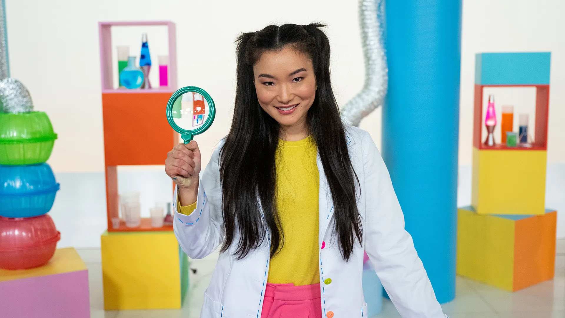 Michelle on the Play School Science Time set, wearing a lab coat, holding a magnifying glass.