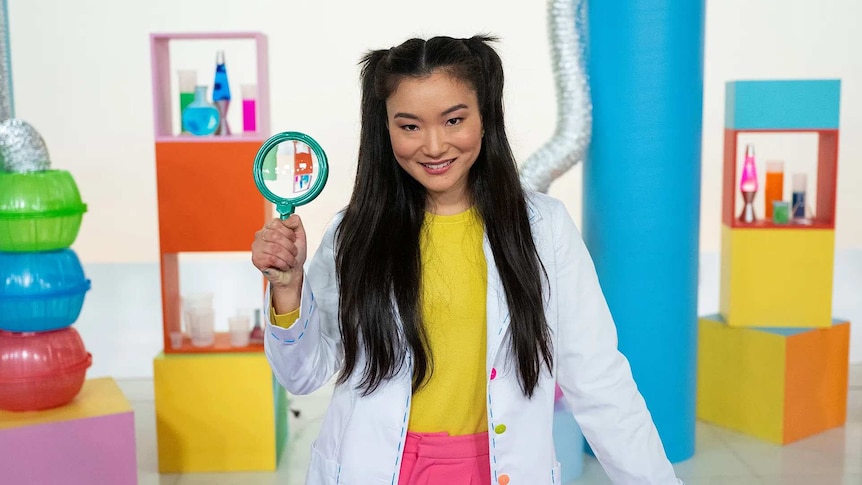Michelle on the Play School Science Time set, wearing a lab coat, holding a magnifying glass.