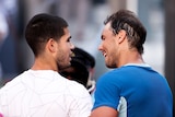 Two tennis players, one wearing white and the other wearing blue, talk after a game