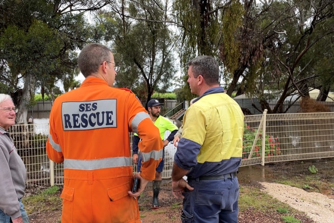 A man in a SES uniform talking to a group of people near a flooded front yard. 