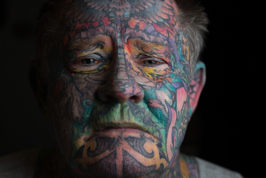 Homeless man John Kenney, whose face is covered in tattoos, poses for a photo.