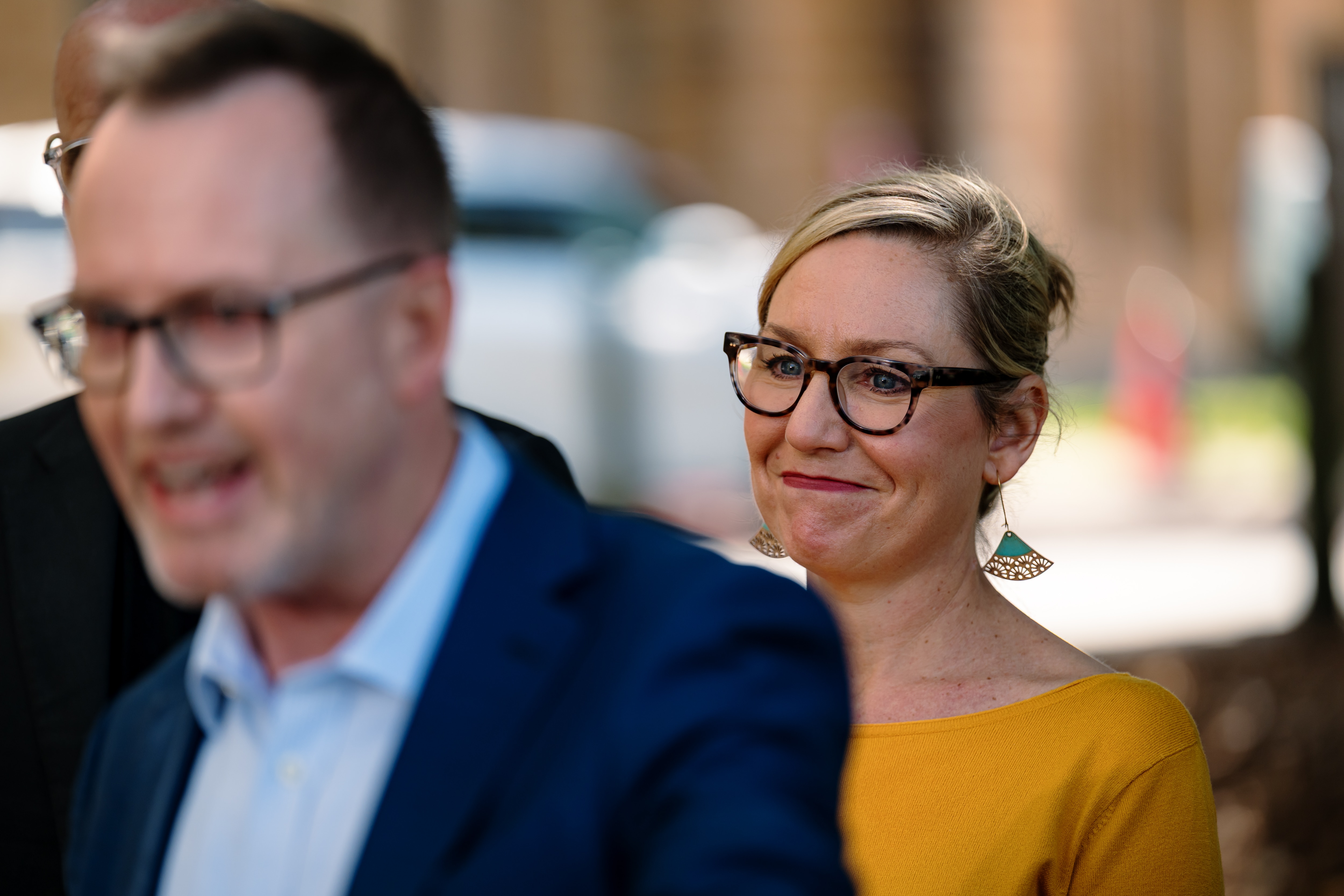 Larissa Waters in sharp focus looking happy and sad as David Shoebridge talks in front of her.