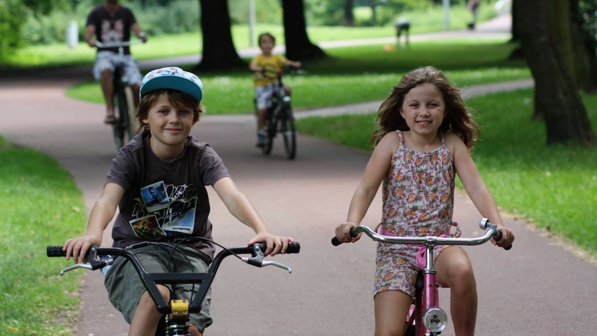 A young boy wearing a hat rides his bike next to his sister who is riding a pink bike