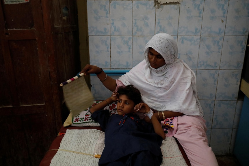 A woman fans her son who is lying in bed.