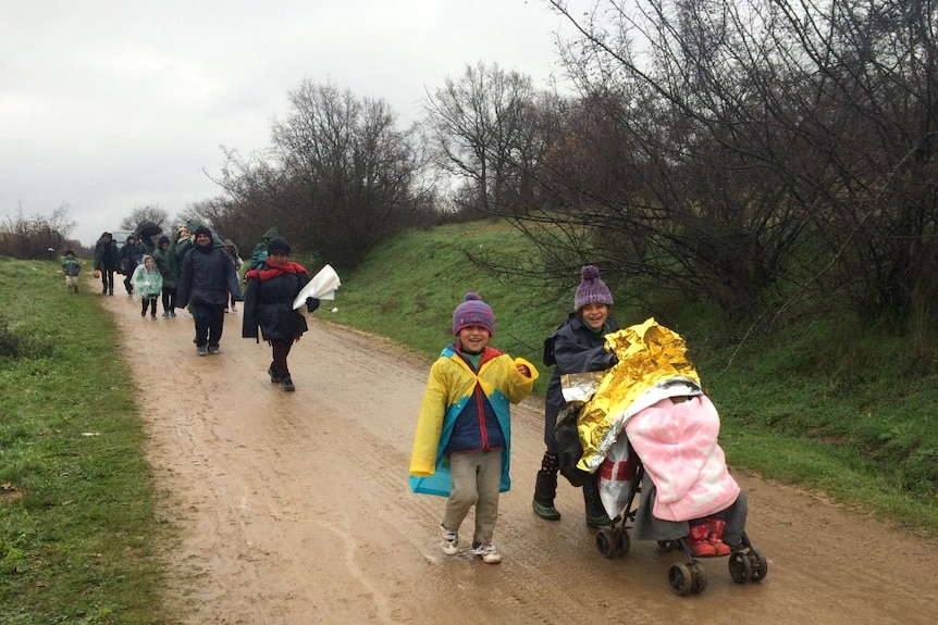 Refugees walk down a muddy rural road.