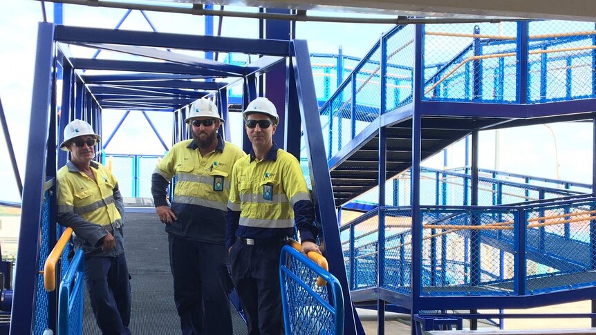 Three men in high-vis workwear stand on the new blue gangway at Broome wharf