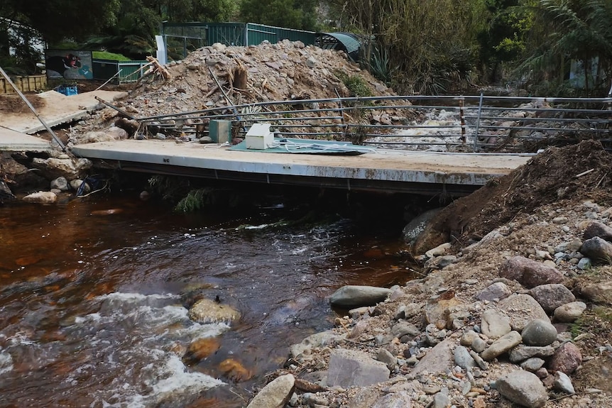 A twisted and damaged concrete footbridge, with creek passing underneath.