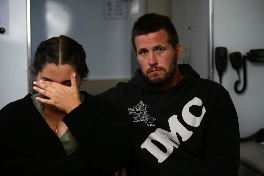 A woman covers her face crying, sitting next to a man who is clearly distressed.