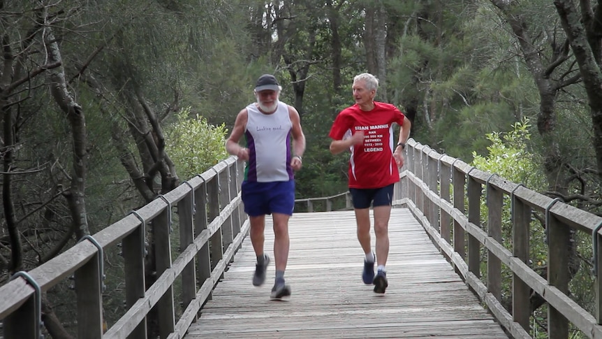 Two older men running over a wooden bridge