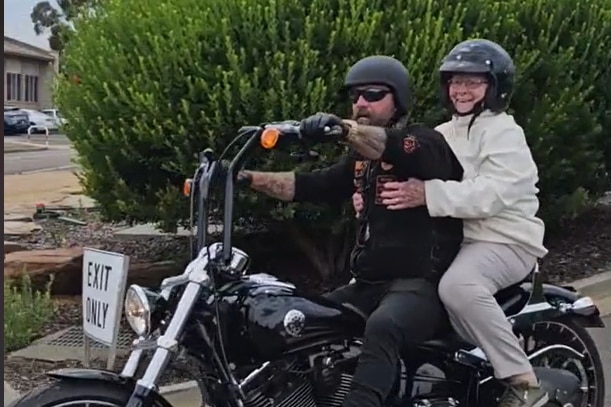 An elderly lady as a pillion passenger on a motorbike.