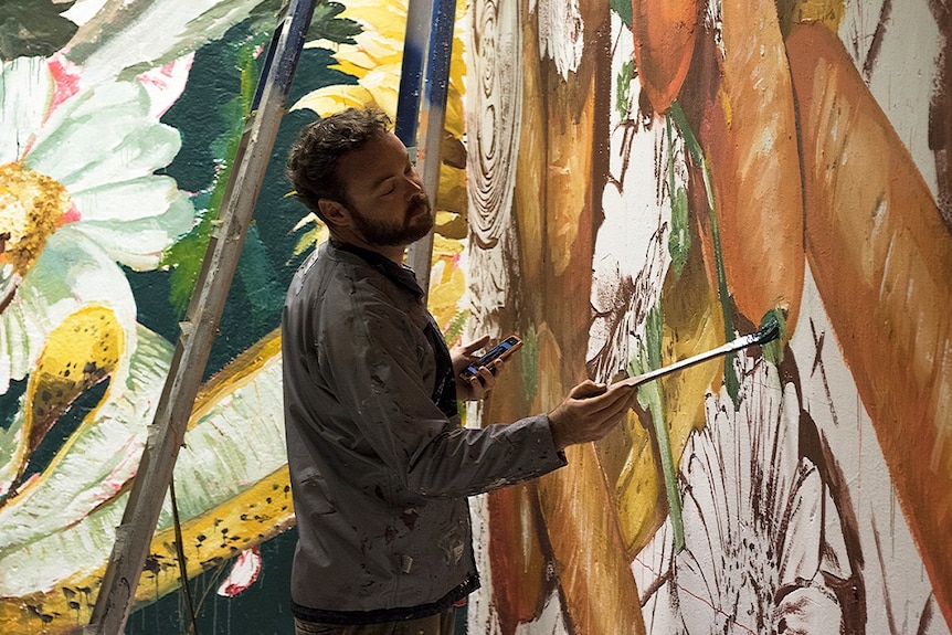 Street artist on a lift paints side of a silo