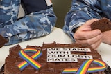 A closeup of a cake with a rainbow ribbon on it and writing saying we stand with our LGBTI mates
