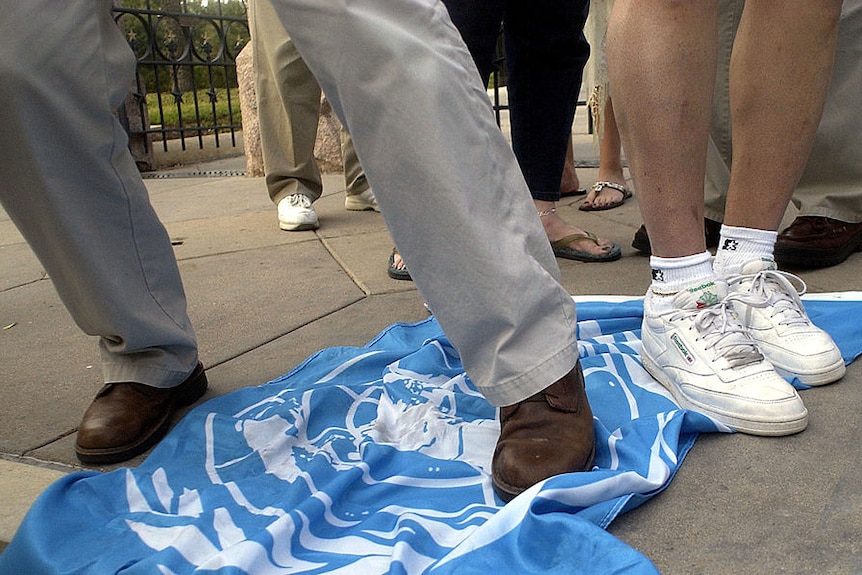 two legs stand on a crumpled UN flag atop a concrete pavement