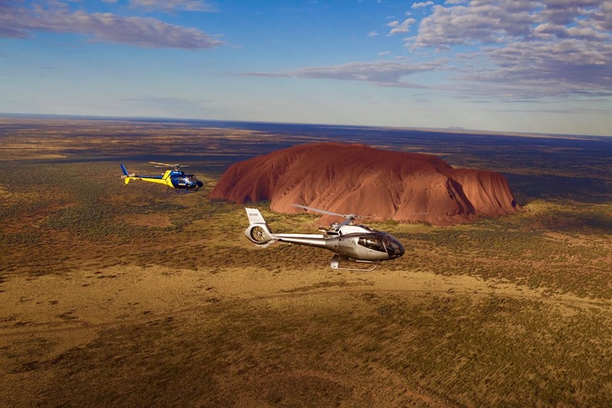 Two aircraft from the Professional Helicopter Services company flies past Uluru.
