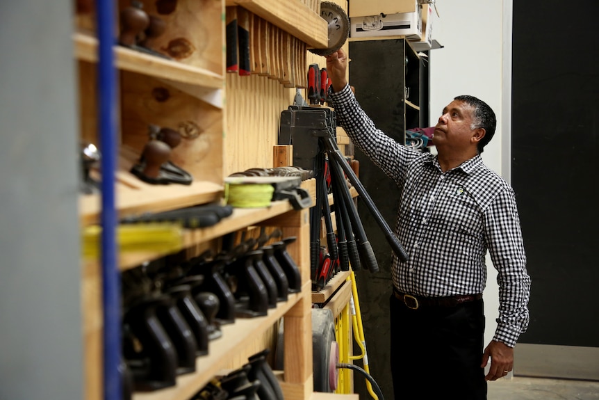 A man stands and looks up at a wall of tools in a workshop.