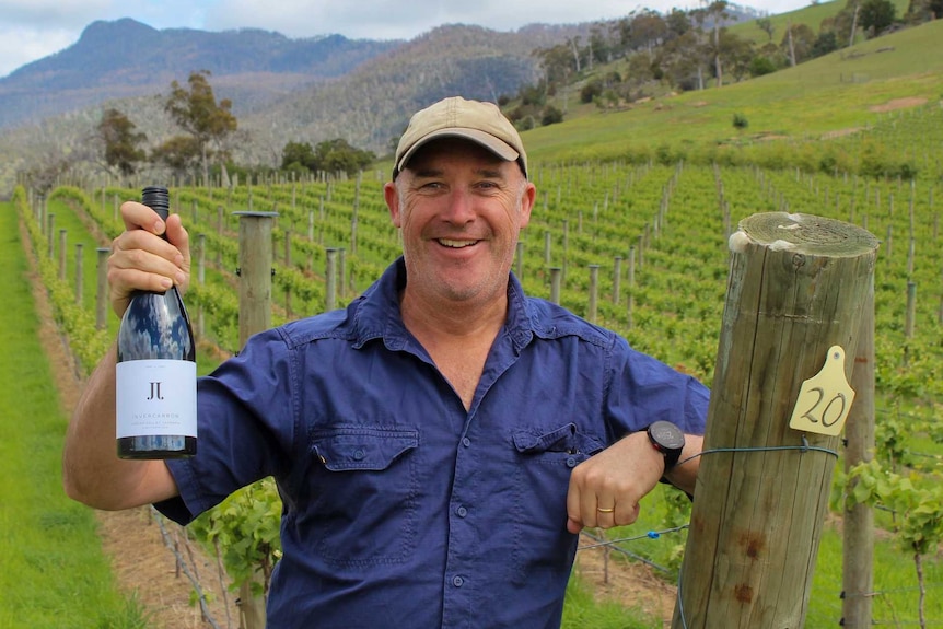 man holding a bottle of wine in a vineyard