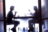 Two people obscured by opaque glass, sit at table.