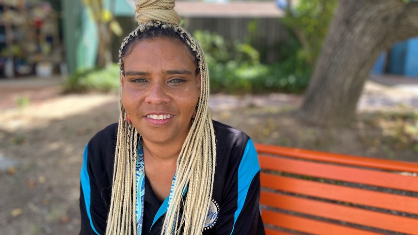 A woman with braids smiles while sitting on a bench
