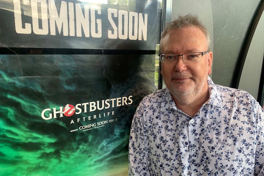 A man standing in a movie theatre against a Ghost Busters poster