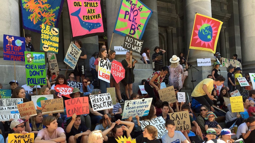 Dozens of students holding colourful signs gather on the steps of the South Australian Parliament.