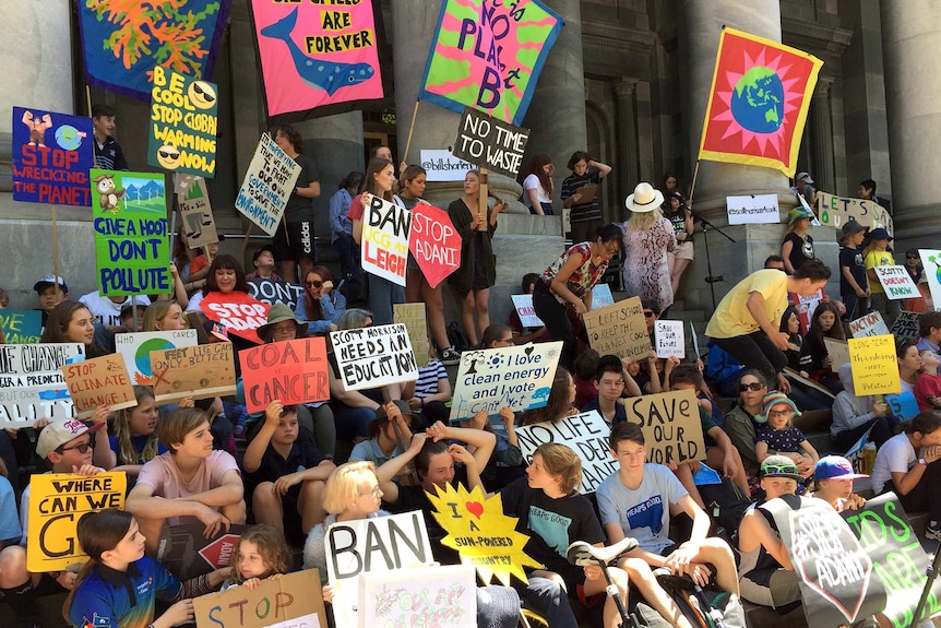 Dozens of students holding colourful signs gather on the steps of the South Australian Parliament.