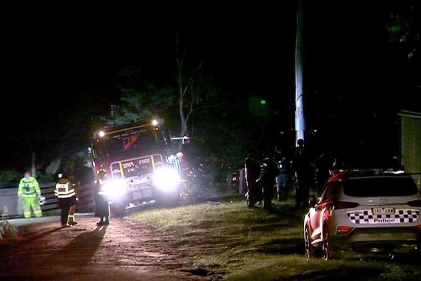 About a dozen emergency services workers stand near a police car and a fire truck at night.