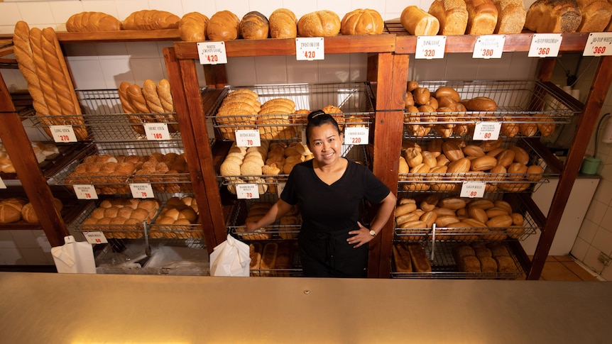 A woman stands behind a counter in a bakery.