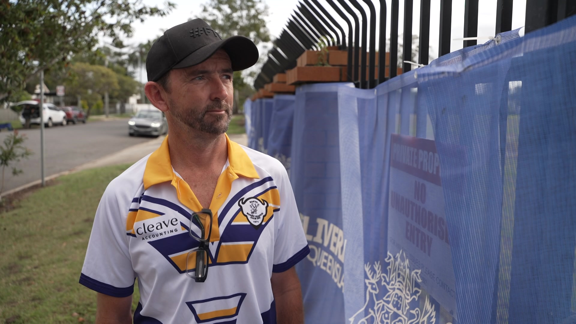 A man in a cap and jersey standing next to construction fence.