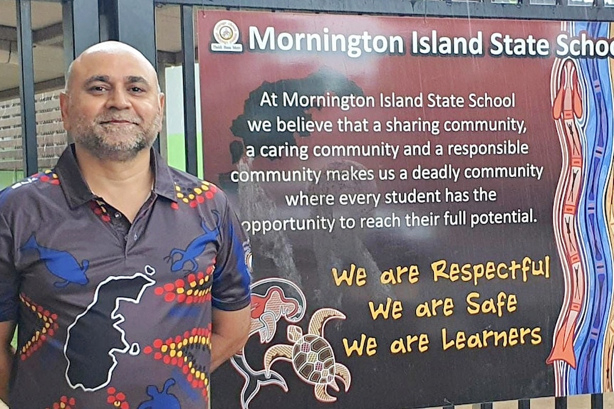 man in colourful shirt stands infront of school