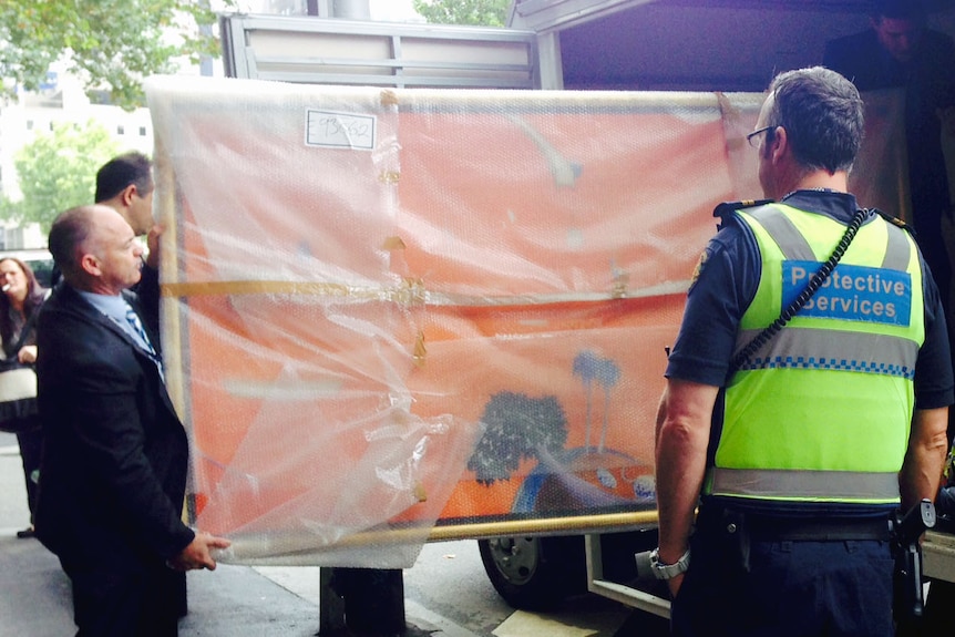 Court staff and a protective services officer carry the Big Orange painting wrapped in plastic into a truck.