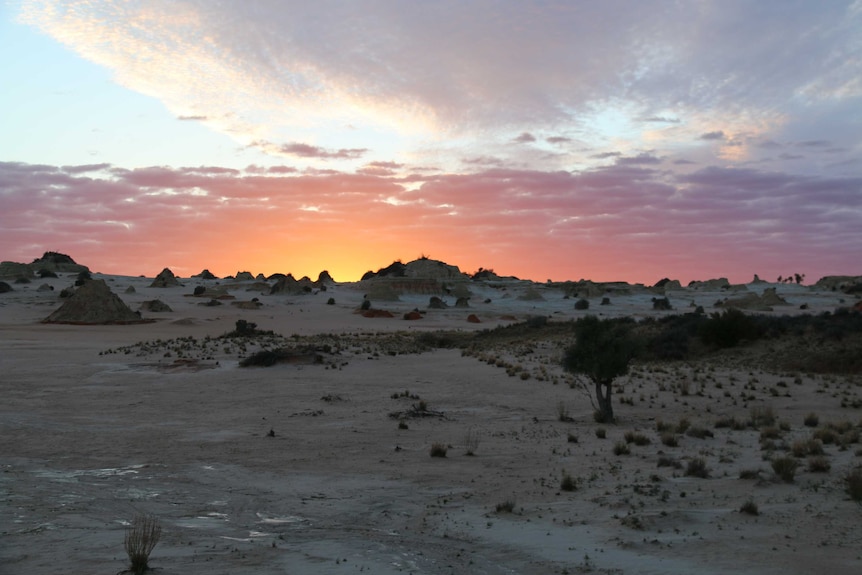 The sunrise lights the sky while silhouetting the landscape.