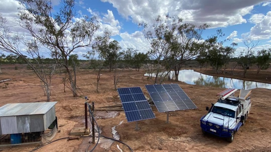 Dam in background with a small shed sitting next to solar panels and a ute in the foreground.