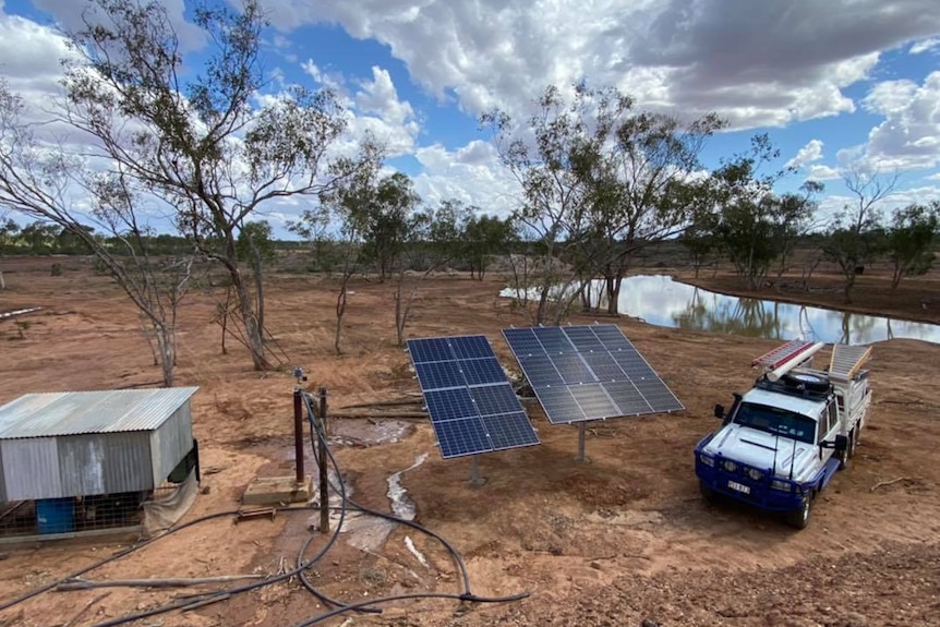 Dam in background with a small shed sitting next to solar panels and a ute in the foreground.