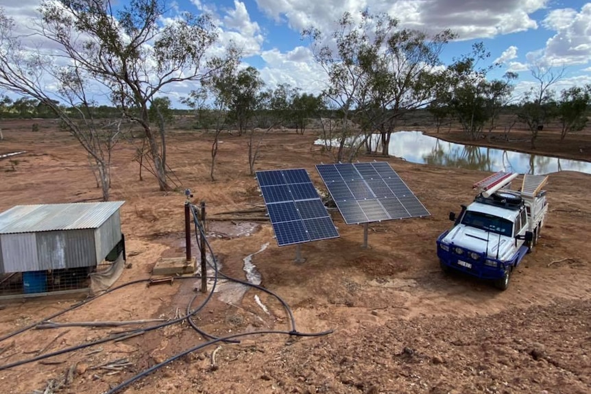 Dam in background with a small shed sitting next to solar panels and a ute in the foreground. 