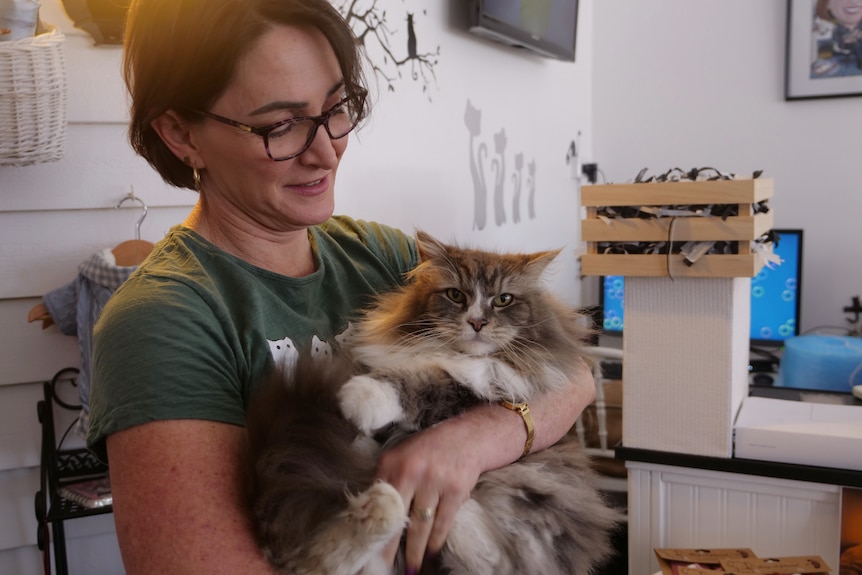 Tracey Austin smiling holding her fluffy brown and white cat Cleo in her arms.