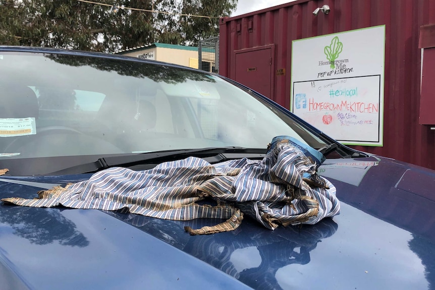 A singed shirt on a car bonnet with a sign for the Homegrown Kitchen behind it.