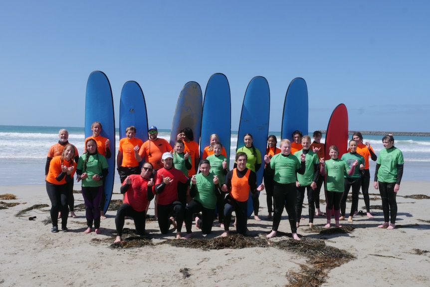 A group of people in wetsuits stand in front of tall surf boards. 