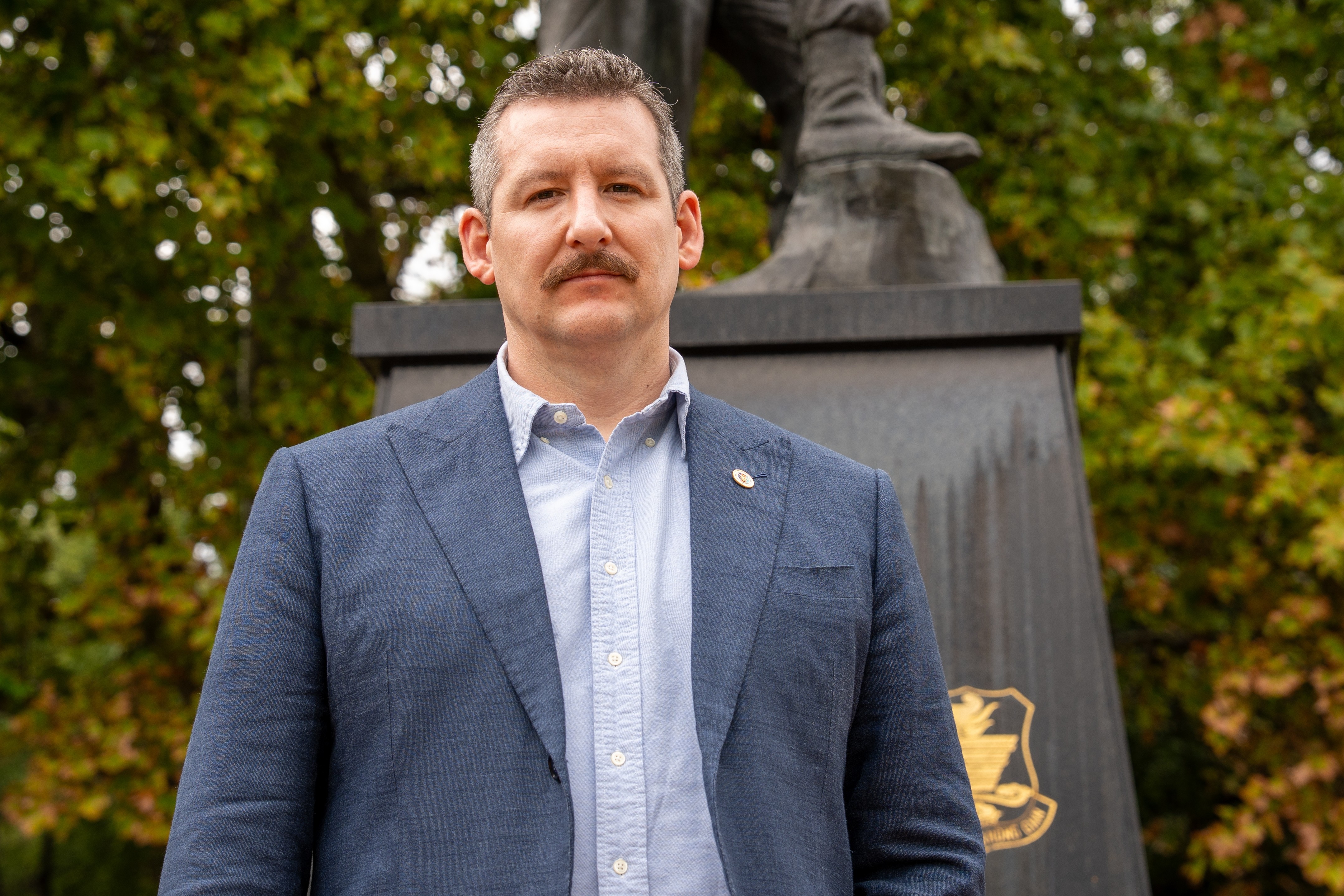 Un hombre con bigote se para frente a un monumento a los caídos