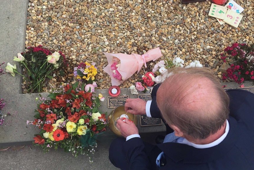 Looking down on bald man lighting candle by grave