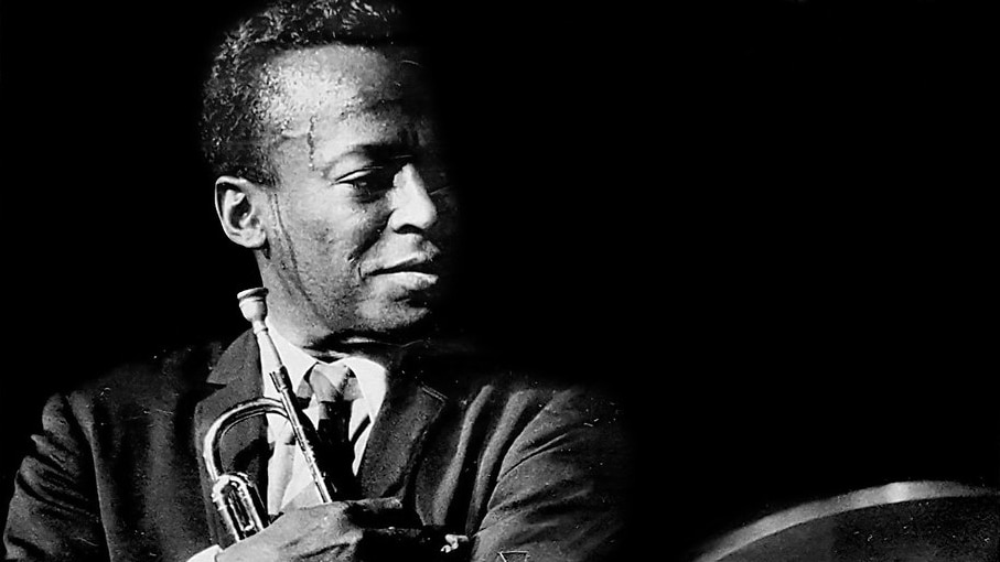 Miles Davis holding his trumpet on stage circa 1964