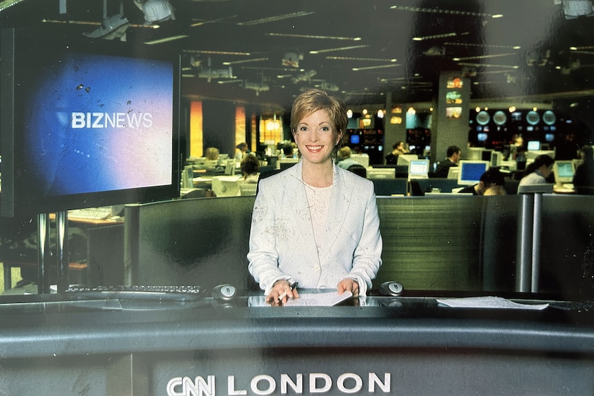 a woman with short hair sitting  behind a desk in a studio preparing to read the news on television