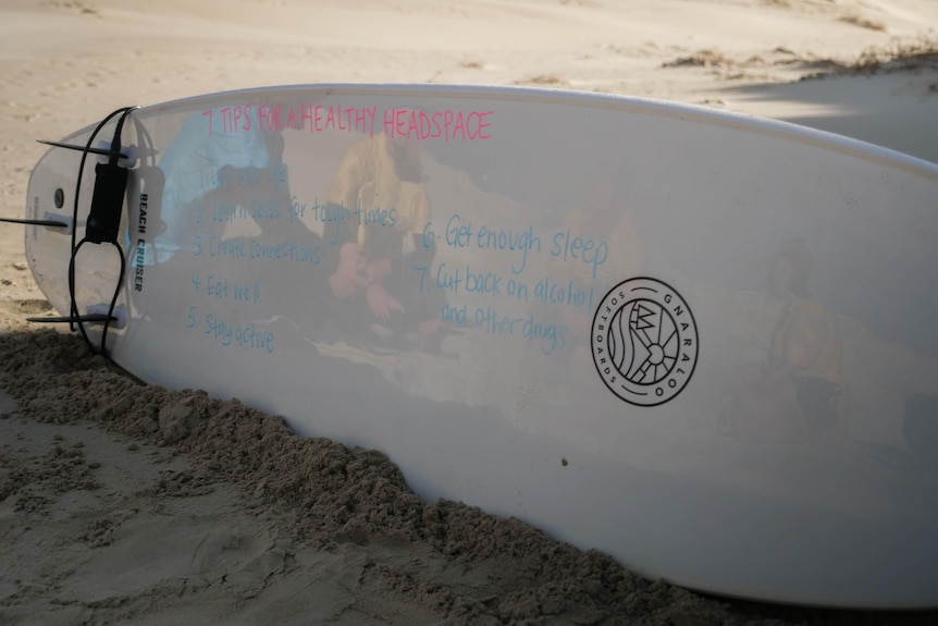 A surfboard on its side with mental health tips written on it