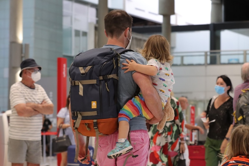 An unidentified man carries a toddler and a walking backpack through Brisbane Airport.
