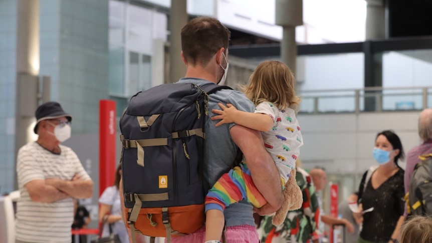An unidentified man carries a toddler and a backpack walking through the Brisbane Airport.