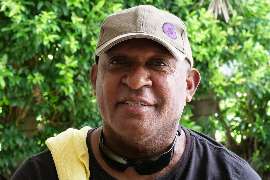 Indigenous man smiling wearing a cap, standing outside.
